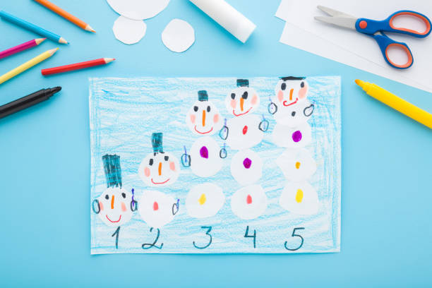 istock Created and decorated snowman shapes and numbers on paper on light blue table background. Pastel color. Closeup. Baby development. Top down view. 2022553154