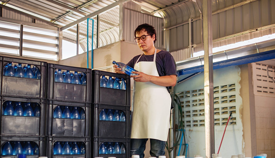 Young Asian man worker wear glasses
working in checking bottled drinking water in drink water factory before shipment.drinking water business.