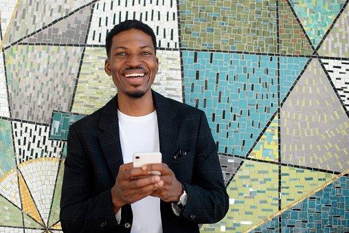 Phone, wall background and portrait of business black man for social media, network and communication. Professional, city and happy person on smartphone for online chat, internet or website in Kenya