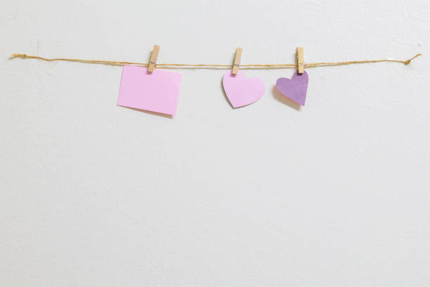 Pink paper cut hearts hanging on a clothesline with wooden clothespins. Blue background, space for copy.