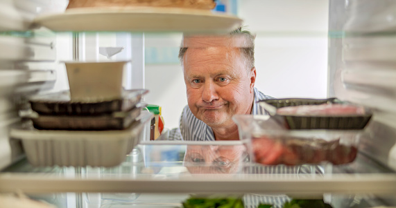 Frowning senior man looking food in refrigerator at kitchen.