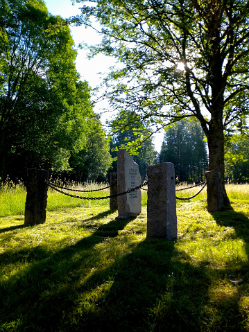 Memorial stone in chained fence on top a sunlit hill with trees overlooking. Close to Soldattorpet, Järbo, Dalsland.