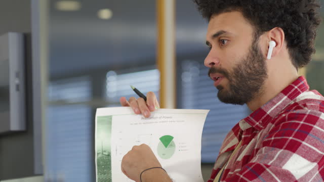 Man holding a paper with graphs and showing it to person over a videocall meeting