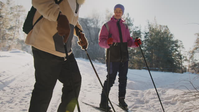 Elderly Caucasian Man Putting on Skis in Forest and Wife Watching
