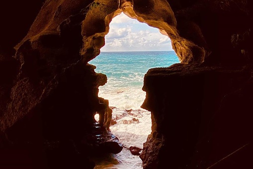 The image depicts the Cave of Hercules in Tangier, showcasing a cave with a beach and water inside. The natural arch formation was created through erosion, providing a picturesque view of the ocean landscape.