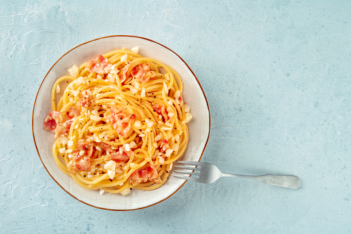 Carbonara pasta dish, traditional Italian spaghetti with pancetta and cheese, overhead flat lay shot with a fork and copy space