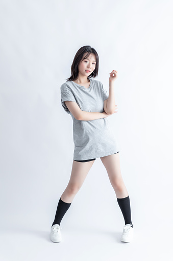 A young Asian woman in a gray t-shirt and black shorts poses on a white background