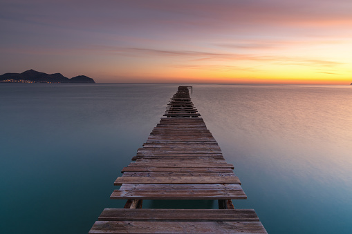 Peaceful sunrise seascape with an old wooden dock leading out into the calm ocean waters