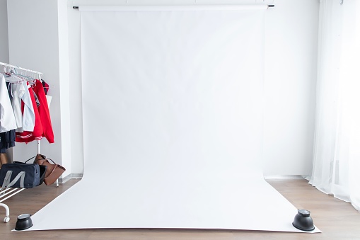 A photo studio with a large white backdrop, a clothing rack with clothes on it, and a brown floor.