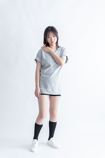 A young Asian woman in a gray t-shirt and black shorts poses with her hand on her shoulder