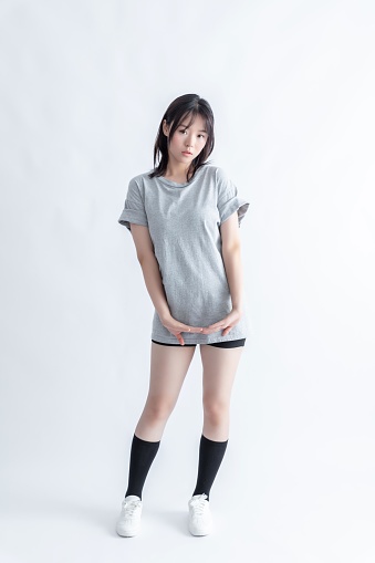A young Asian woman in a gray t-shirt and black shorts poses with her hands clasped in front of her.