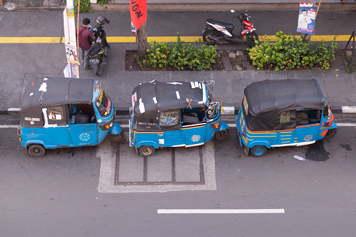 Jakarta, Indonesia - February 08, 2024: Row of bajaj parked on the side of the road in Jakarta. Waiting for passenger. Blue Bajaj is a three-wheeled public transportation.