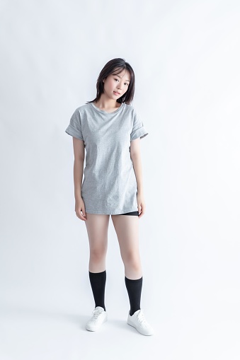 A young woman in a gray t-shirt and black shorts poses against a white background