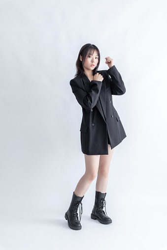 Asian young woman in black suit and boots posing on white background