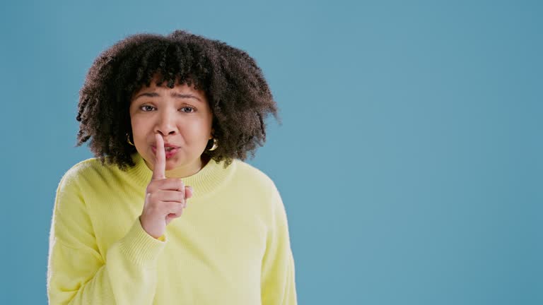 Woman, finger and face for privacy in studio, mockup space and confidential information or emoji. Female person, portrait and shush for quiet on blue background, closeup and silence for announcement