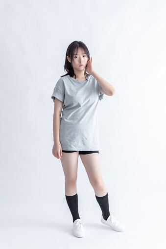 A young Asian woman in a gray t-shirt and black shorts poses against a white background