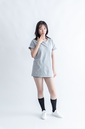 A young Asian woman in a gray t-shirt and black shorts is standing with her hand covering her mouth