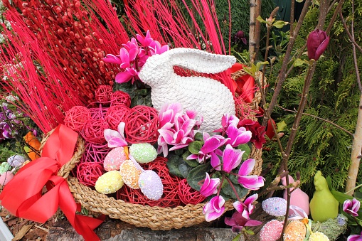 White bunny, flowers, ribbons and eggs on rattan basket decor on streets of the city. Easter decor in rustic style. Easter holiday decoration of the central square. Happy Easter concept