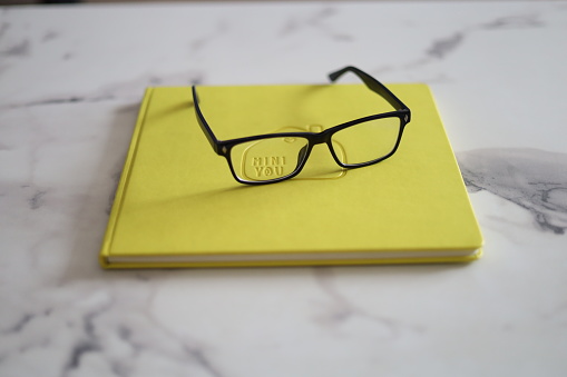 A pair of stylish glasses rests atop a well-loved yellow book.