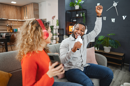 Happy multiracial couple having fun singing karaoke at home