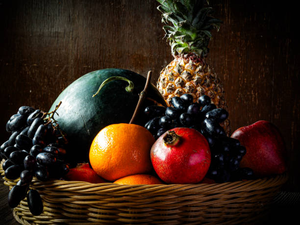 The assorted fruits in a basket on old wooden table against walnut brown backdrop.