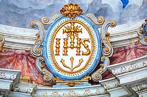 architectural gilded volumetric composition of the initials of Jesus Christ in a church interior