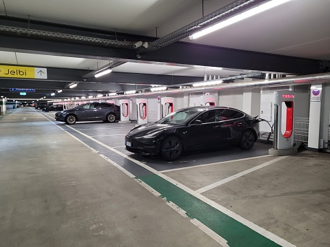 Berlin, Germany - Jan 07, 2024: A static shot of a solid black Tesla Model 3 dual motor charging at the Berlin Supercharger in a covered parking lot. Selective focus