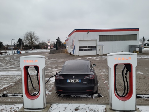 Gutzkow, Germany - Jan 09, 2024: A static shot of a solid black Tesla Model 3 dual motor charging at the Gutzkow Supercharger in a cloudy winter day. Selective focus