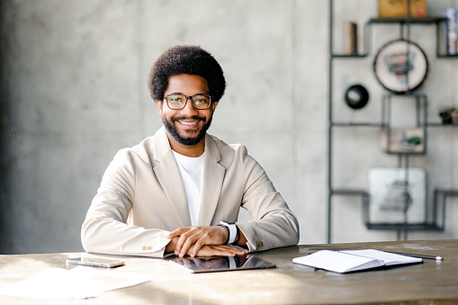 Brazilian businessman with genial smile radiates as he sits at a desk, representing the seamless blend of professionalism and comfort in the business environment. Portrait of employee on the workplace