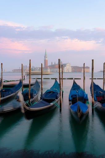 A beautiful sunset illuminates a line of gondolas tied up on the side of the Grand Canal in Venice. Across the lagoon we see the iconic shape of the Church of San Giorgio Maggiore.