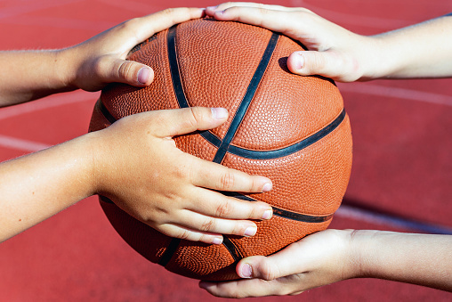 Basketball ball in the hands of a two kids,red court outdoors background.Closeup.