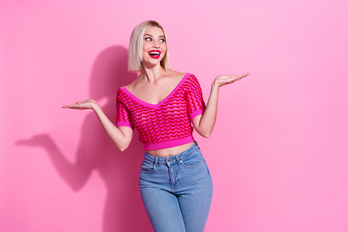 Portrait of impressed nice woman with bob hairdo dressed knit top arms demonstrate products look empty space isolated on pink background.