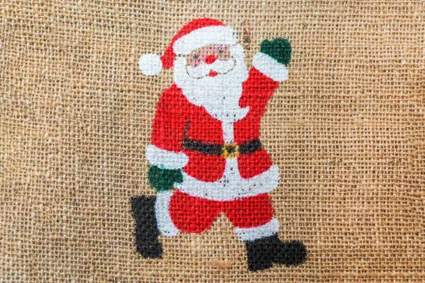 Photo of homemade small christmas decorative Santa Claus on the jute hessian sackcloth canvas sack cloth woven texture pattern background