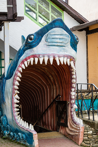 Entrance to oceanarium through huge open mouth of shark in Arkhipo-Osipovka. Close-up. Pointed nose, bulging eyes huge white teeth and wide-open mouth. Gelendzhik, Russia - May 16, 2021