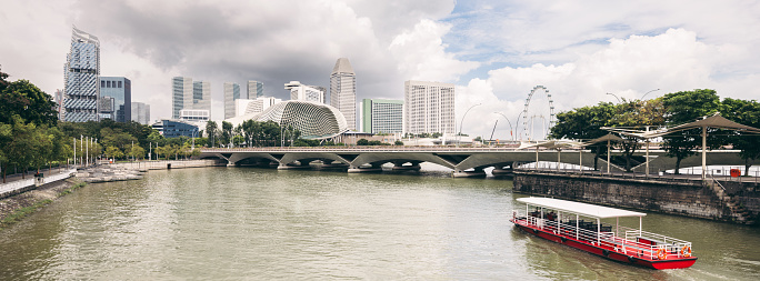 Singapore River Cityscape Panorama with typical red tourist sightseeing tour boat cruising on Singapore River towards Pedestrian Jubilee Bridge - Footbridge and the famous Singapore Marina Bay. XPAN Crop Urban City Panorama. Singapore, Southeast Asia