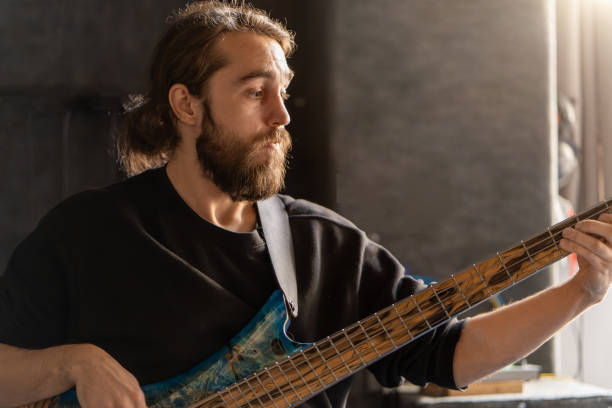 man with beard plays bass guitar. his fingers move quickly along the strings, creating music. musician focused and in moment, showcasing his passion for music - plucking an instrument imagens e fotografias de stock