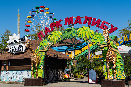Malibu theme park for adults and children in Arkhipo-Osipovka. Arch of entrance to park. In background there is Ferris wheel. Close-up. Krasnodar Territory, Russia - May 14, 2021