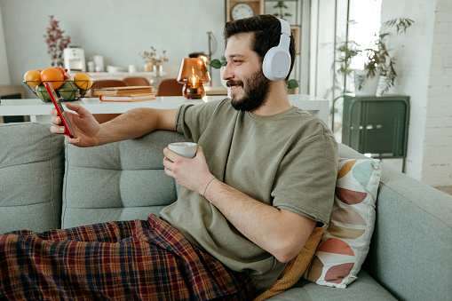 Man wearing wireless headphone and using smart phone on sofa.