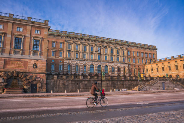 a person cycling infront of the royal palace in stockholm, sweden, in the old town. clear winter day, morning sunlight. - stadsholmen imagens e fotografias de stock