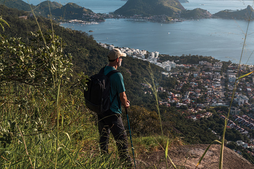 A man stands on a hilltop with a trekking pole, gazing at the breathtaking landscapes below him