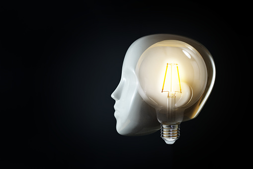 White head of a mannequin with a glowing light bulb in the brain, concept for thoughts, mind, ideas and creativity or for artificial intelligence, black background, copy space, selected focus