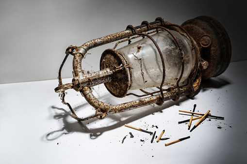 Old rusty kerosene lamp and burnt matches lying on a gray background, symbolizing outdated concepts that are no longer in keeping with the times, copy space, selected focus