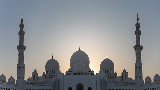 Abu Dhabi, United Arab Emirates - March 08, 2017:  Panorama of the domes and minarets of Sheikh Zayed Grand Mosque, with the setting sun as a backlight