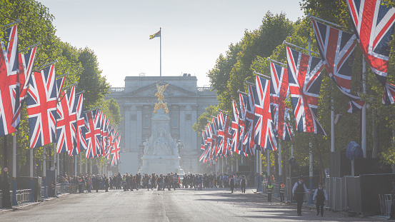 London, England, United Kingdom - September 17, 2022: The Mall lined with Union Jack flags in front of Buckingham Palace with 2 policemen and a small crowd crossing - preparations for the funeral of Queen Elizabeth II