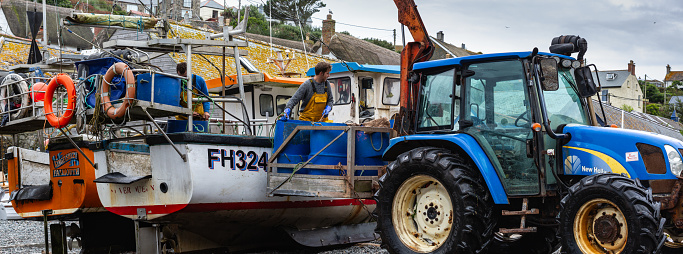 Panorama of Two fishermen unloading their catch of crabs onto a tractor in the village of Cadgwith, Lizard Peninsula, Cornwall