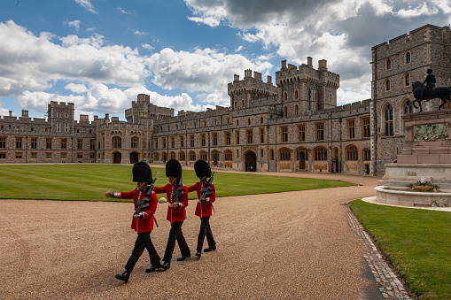 Windsor, England, United Kingdom - July 22, 2011: Three soldiers  carrying guns marching in the courtyard of Windsor Palace in their traditional costume and Bearskin helmets against a blue sky with brightly lit clouds.