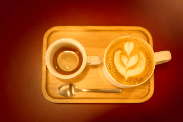 Close up hot coffee latte or cappuccino coffee in mug with heart shape latte art on red table background. Flat-lay, top view. Cup of coffee with flowing milk. Copy space ,food and drink concept. In some other place in the world, these also called Flat Whites.
