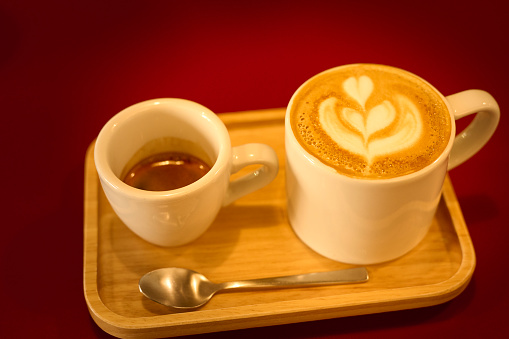 Close up hot coffee latte or cappuccino coffee in mug with heart shape latte art on red table background. Flat-lay, top view. Cup of coffee with flowing milk. Copy space ,food and drink concept. In some other place in the world, these also called Flat Whites.