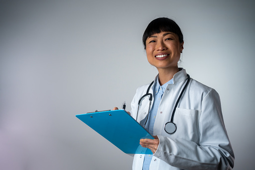 Portrait happy Asian woman doctor on white background with clipboard writing. Confident Japanese female doctor isolated. Smiling Asian medical doctor with clipboard
