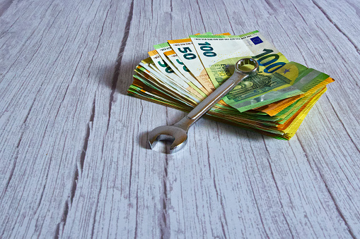 A stack of banknotes with a wrench on a wooden background, horizontal